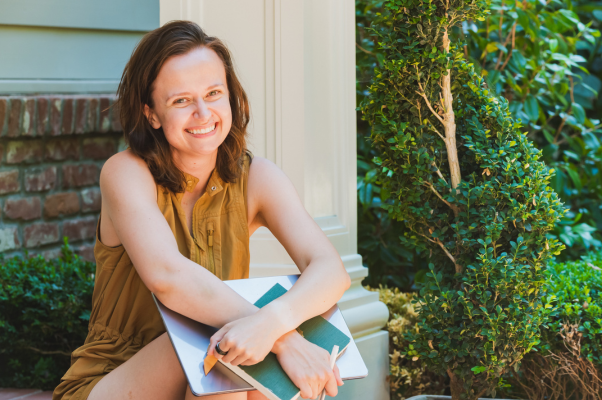 Amanda Lien, Founder of Minutiae Content Co., sits on her front porch with a laptop and diary in her arms